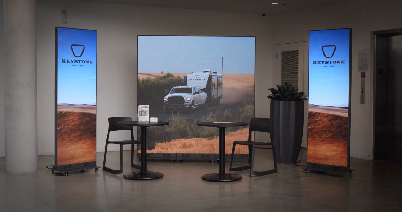 Keystone RV lounge: a video wall flanked by two LED totems, with café tables in front